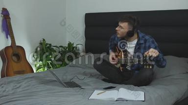 吉他老师调吉他弦.. 戴耳机的年轻人在家里的床上调整电吉他。 有吉他的男音乐家